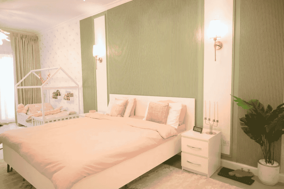 The serene bedroom features soft pink bedding, a house-shaped crib, and green accent walls.