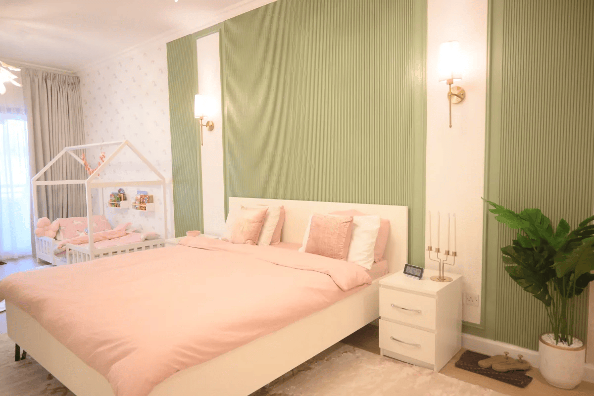The serene bedroom features soft pink bedding, a house-shaped crib, and green accent walls.