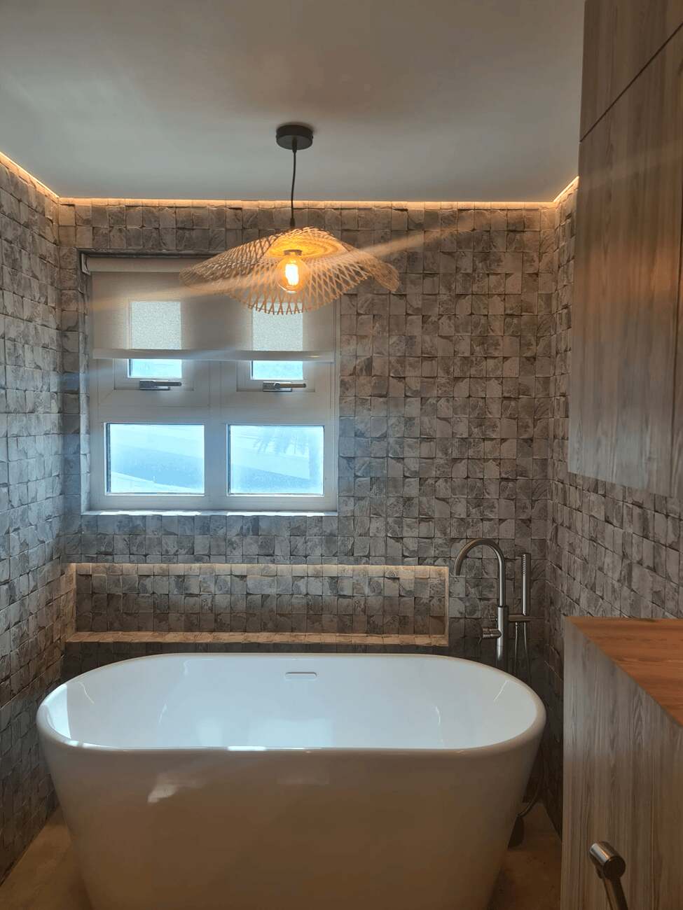 A modern freestanding bathtub in a stylish, minimalist bathroom with natural stone walls and lighting.