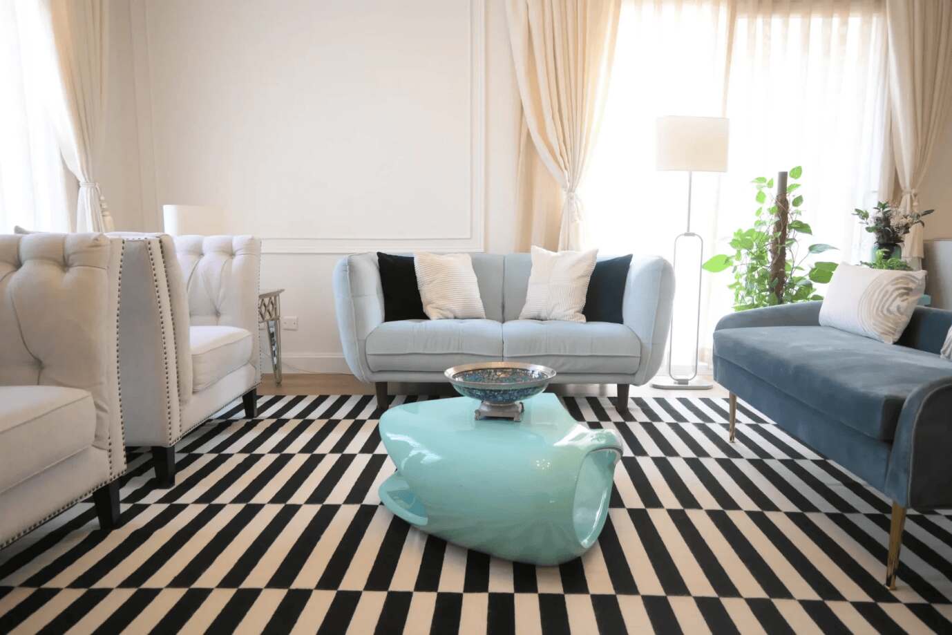 This modern living room features a sky-blue table, neutral tones, and bold striped rug with a unique centerpiece.
