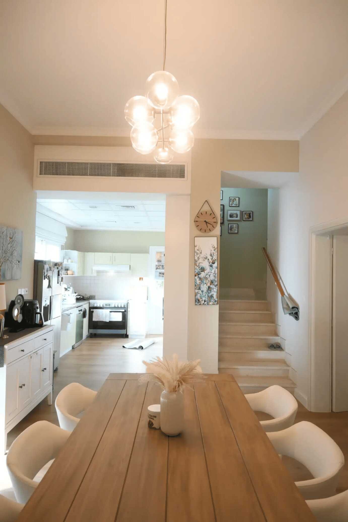 The design is modern with a wooden table, white chairs, and a stylish cluster pendant light.