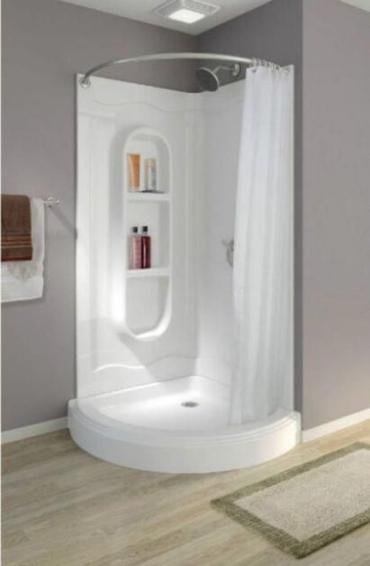 Compact corner shower with a white curved base, built-in shelves for toiletries, a curved shower curtain rod, and light gray walls with wood-style flooring.