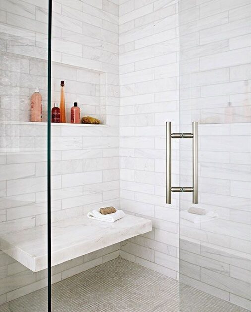 Modern walk-in shower with white subway tiles, built-in bench, glass door, and recessed shelf for toiletries.