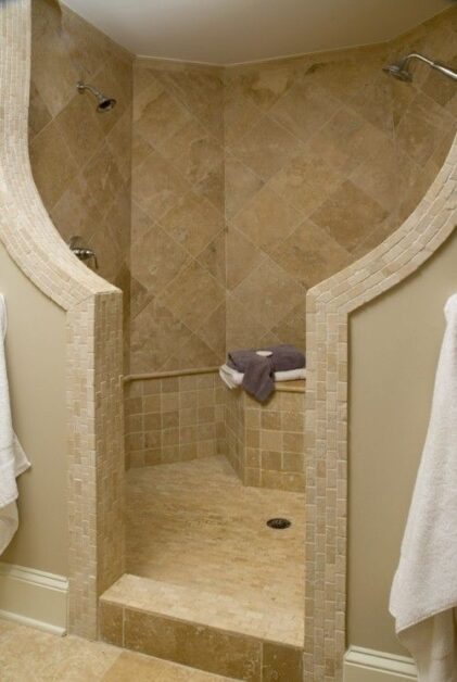 Small bathroom walk-in shower with beige stone tiles, built-in bench, and open entry design.
