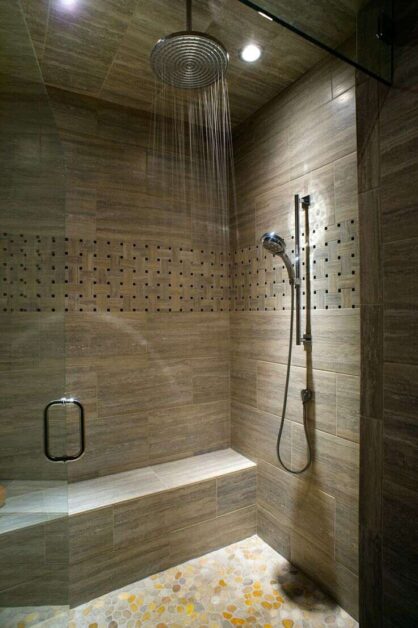 Modern walk-in shower with rainfall showerhead, handheld shower, built-in bench, and tiled walls with accent design.