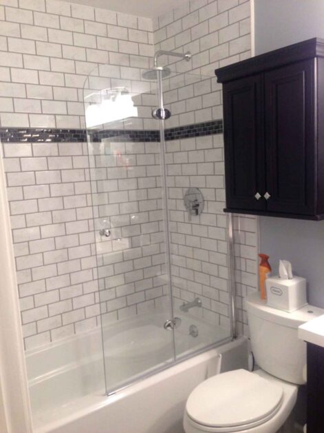 Small bathroom design with bathtub shower combo, glass sliding doors, white subway tile walls, and modern fixtures.